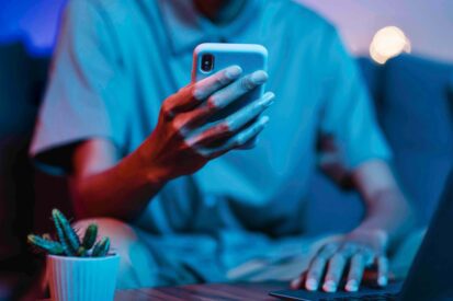 Junger Mann sitzt vor dem Laptop und hat sein Handy in der Hand