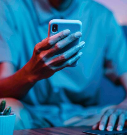 Junger Mann sitzt vor dem Laptop und hat sein Handy in der Hand